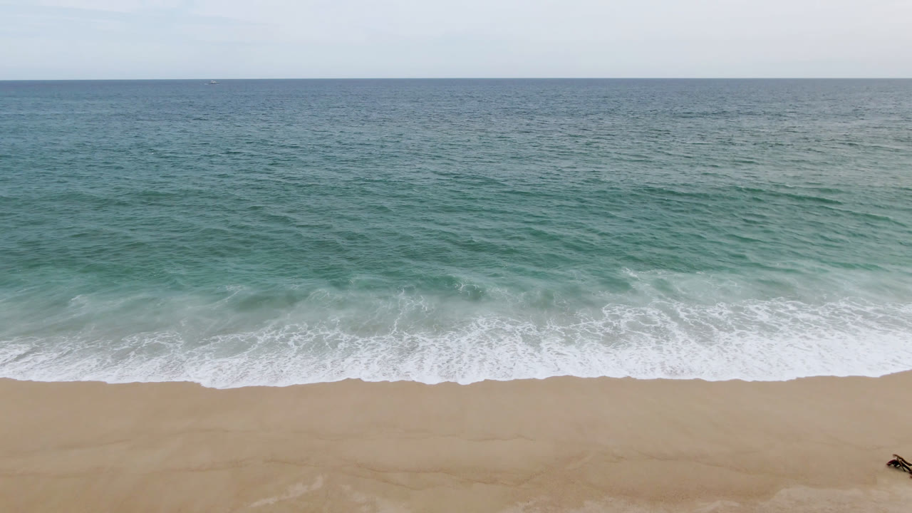 Ocean waves wash toward a sandy beach with a tiny figure at the lower edge.