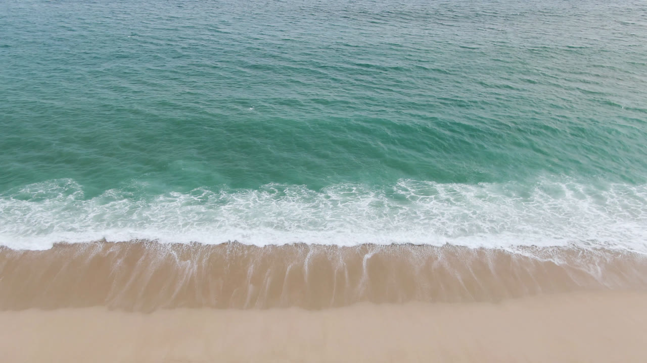 Overhead view of green-blue ocean surf meeting tan sand.