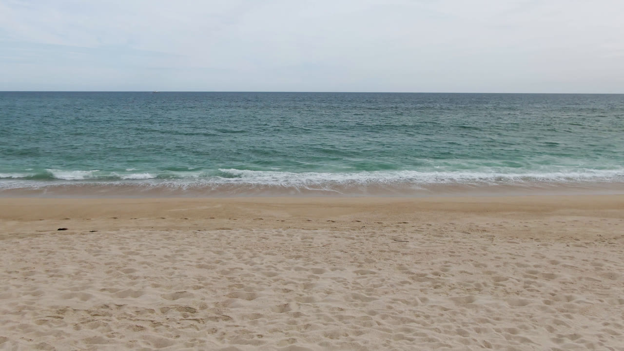 Wide coastal frame from San Jose del Cabo with broad sand, gentle surf, green-blue water, pale sky, and no visible people.