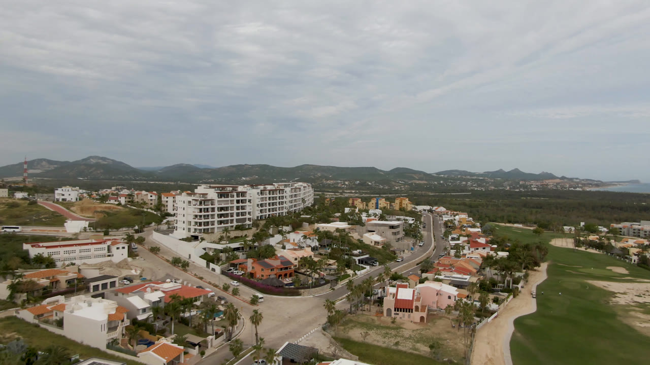 Aerial cityscape with golf course, residential buildings, roads, hills, and distant coast