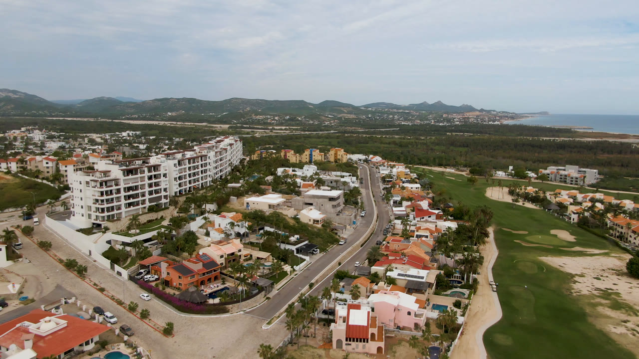 Aerial view of golf course, roads, homes, hills, and distant coast.