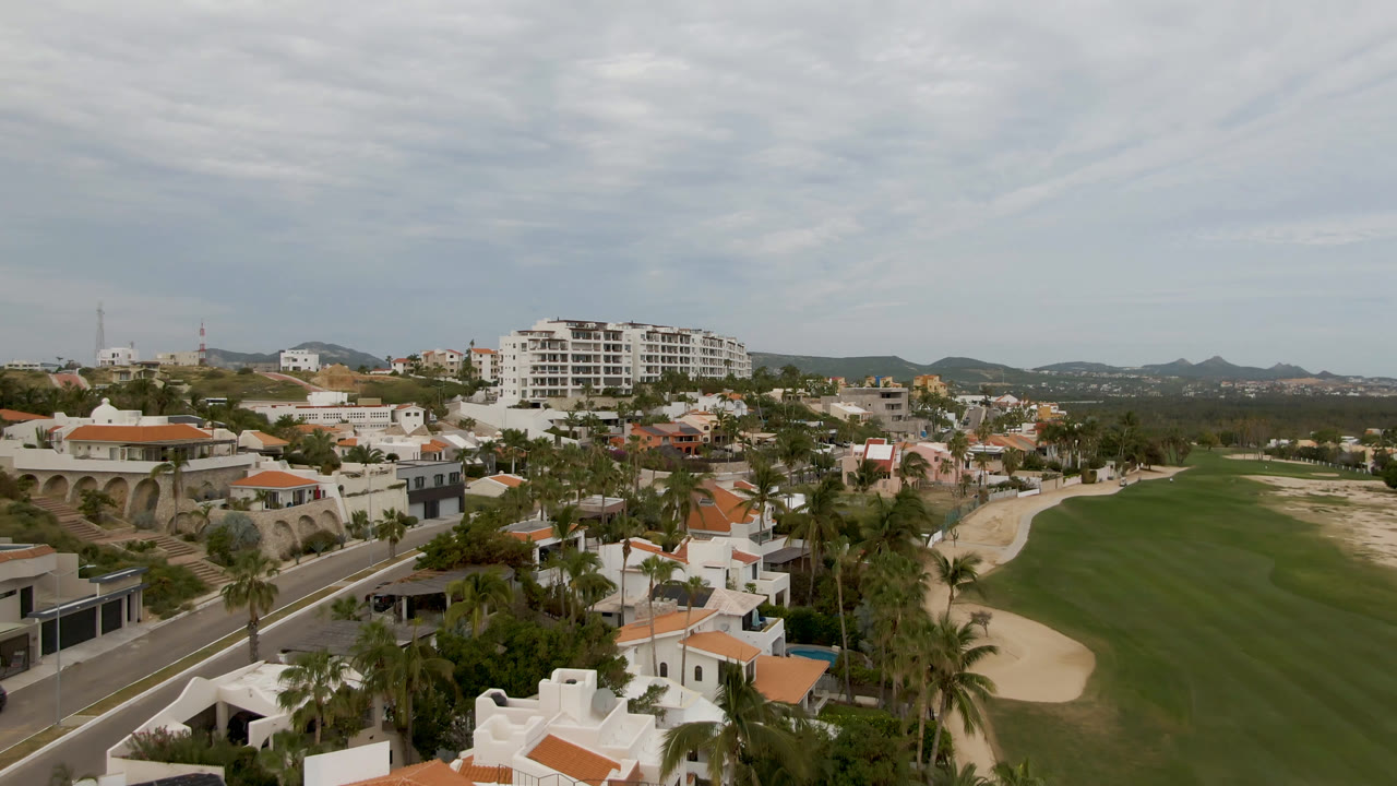 Aerial view over a golf course, road, palms, and white homes with orange roofs.