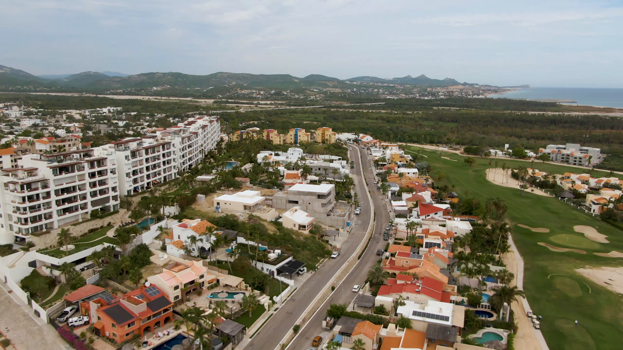 Aerial view of homes, road, golf course, hills, and coastline