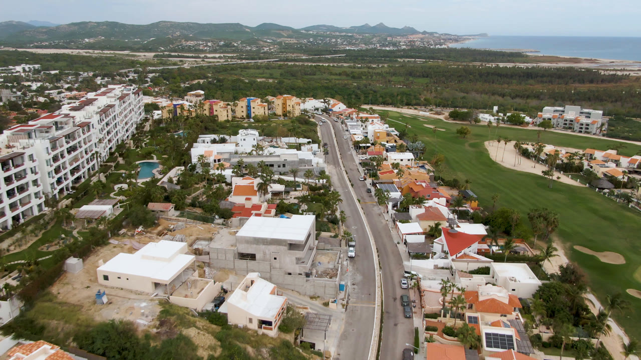 Aerial view of a curved road, homes, apartment blocks, and a golf course near the coast.