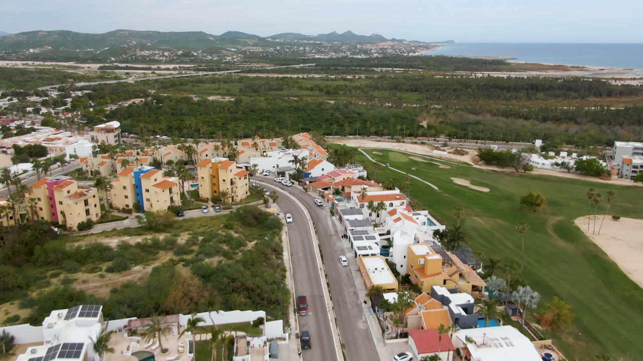 Aerial view of a golf course, coastal neighborhood, road, hills, and ocean.