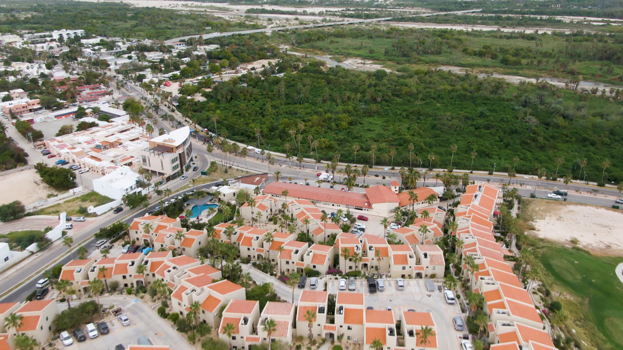 Aerial view of orange-roofed buildings, roads, vehicles, and green terrain.