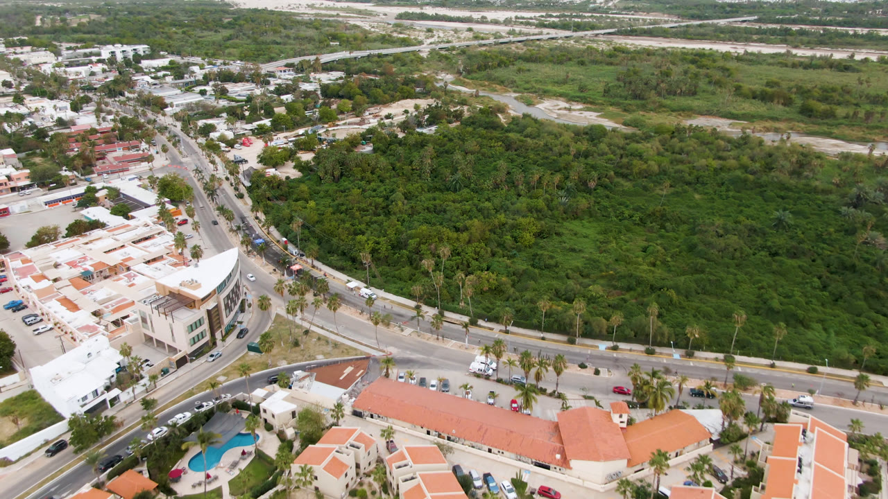 Aerial view of curved roads, low buildings, orange roofs, and dense green land.