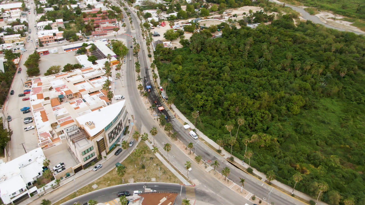Aerial city-edge view with cars on roads and a wooded area.