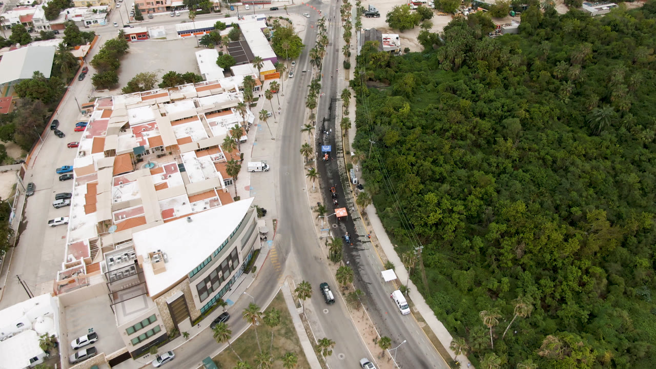 Aerial view of a white building beside a curved road and dense trees.