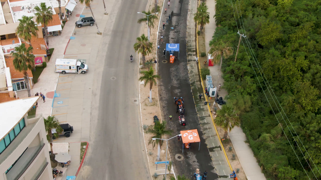 Overhead road with palm trees, tents, parked vehicles, and dense greenery.