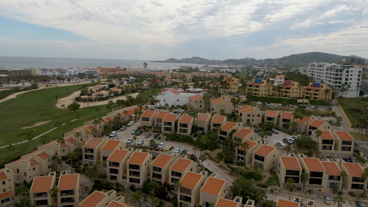 Aerial view of red-roofed homes beside a green golf course and coast