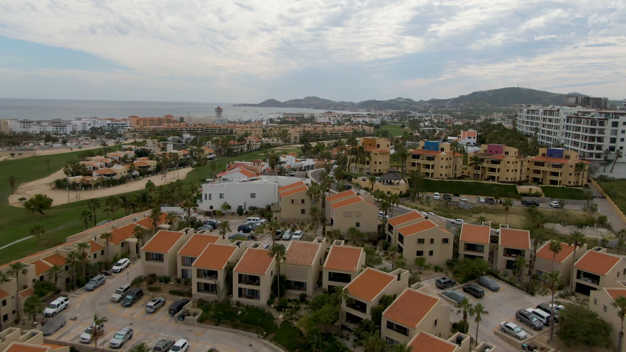 Drone view over terracotta-roof villas, roads, golf course, and distant ocean