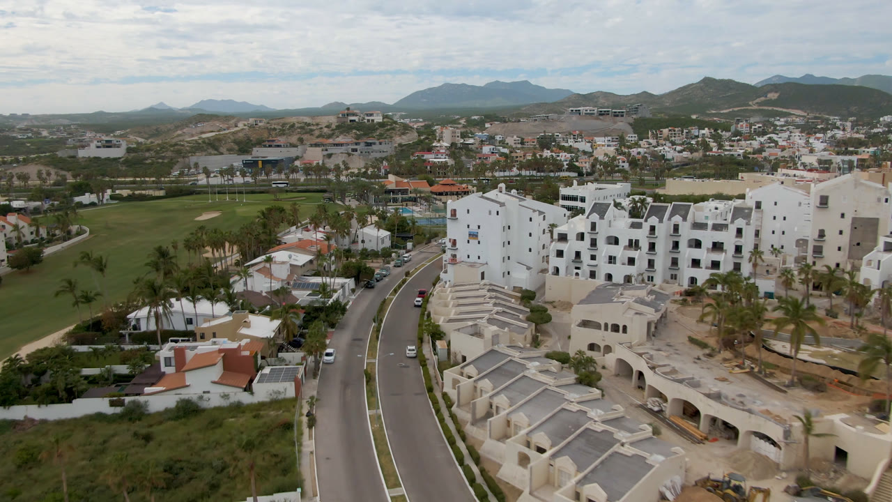 Aerial view of a curving road beside white buildings and a golf course.