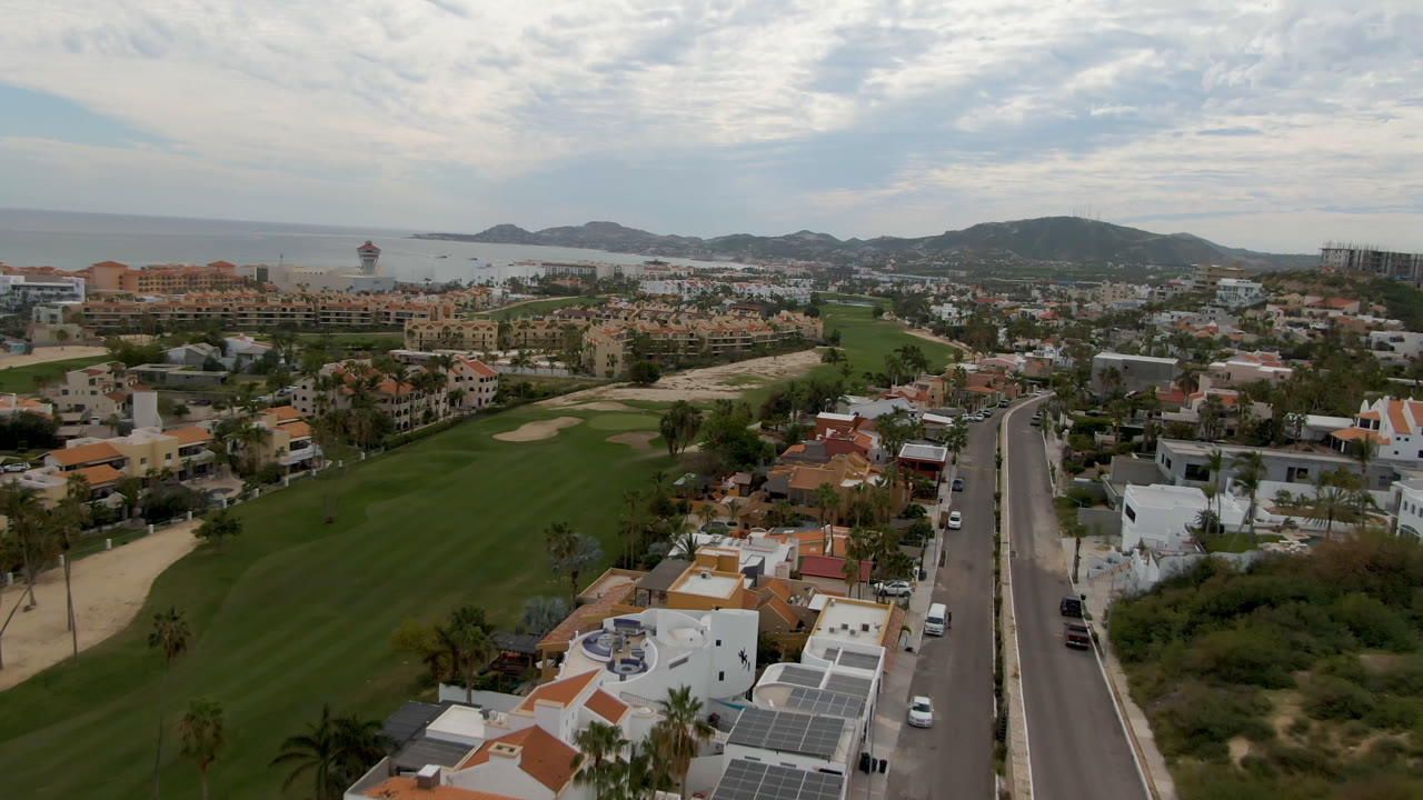 Wide aerial of fairways, villas, roadway, coastline, and hills