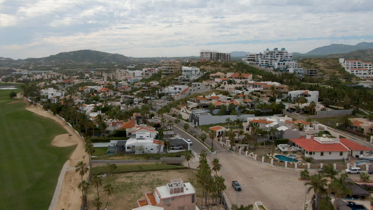 Aerial view of a golf fairway beside houses and palm-lined roads.