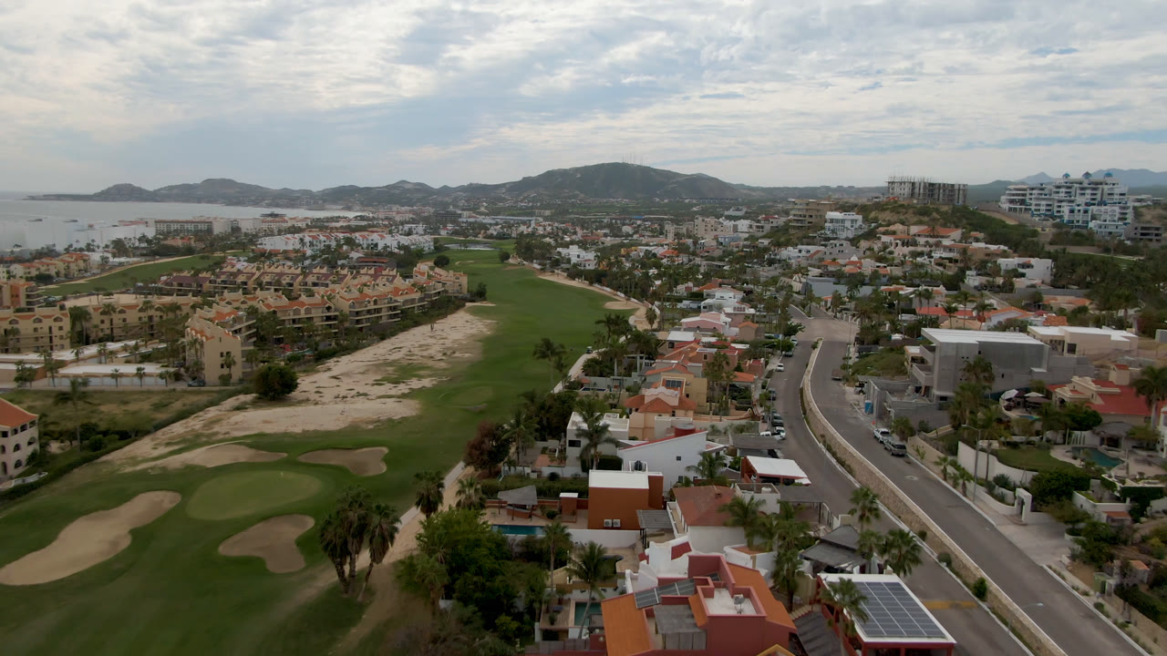 Aerial view across golf greens, villas, ocean shoreline, and cloudy sky.