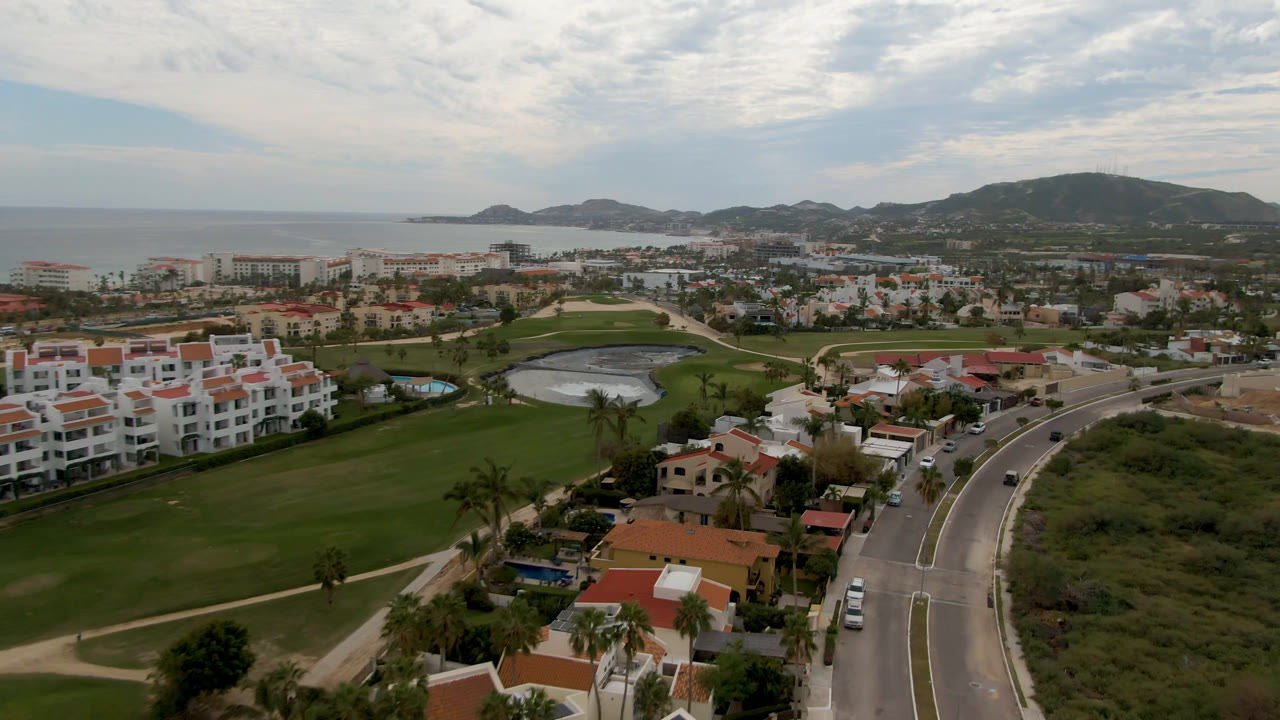 Aerial view of golf course, residential roads, and coastline under cloudy sky.