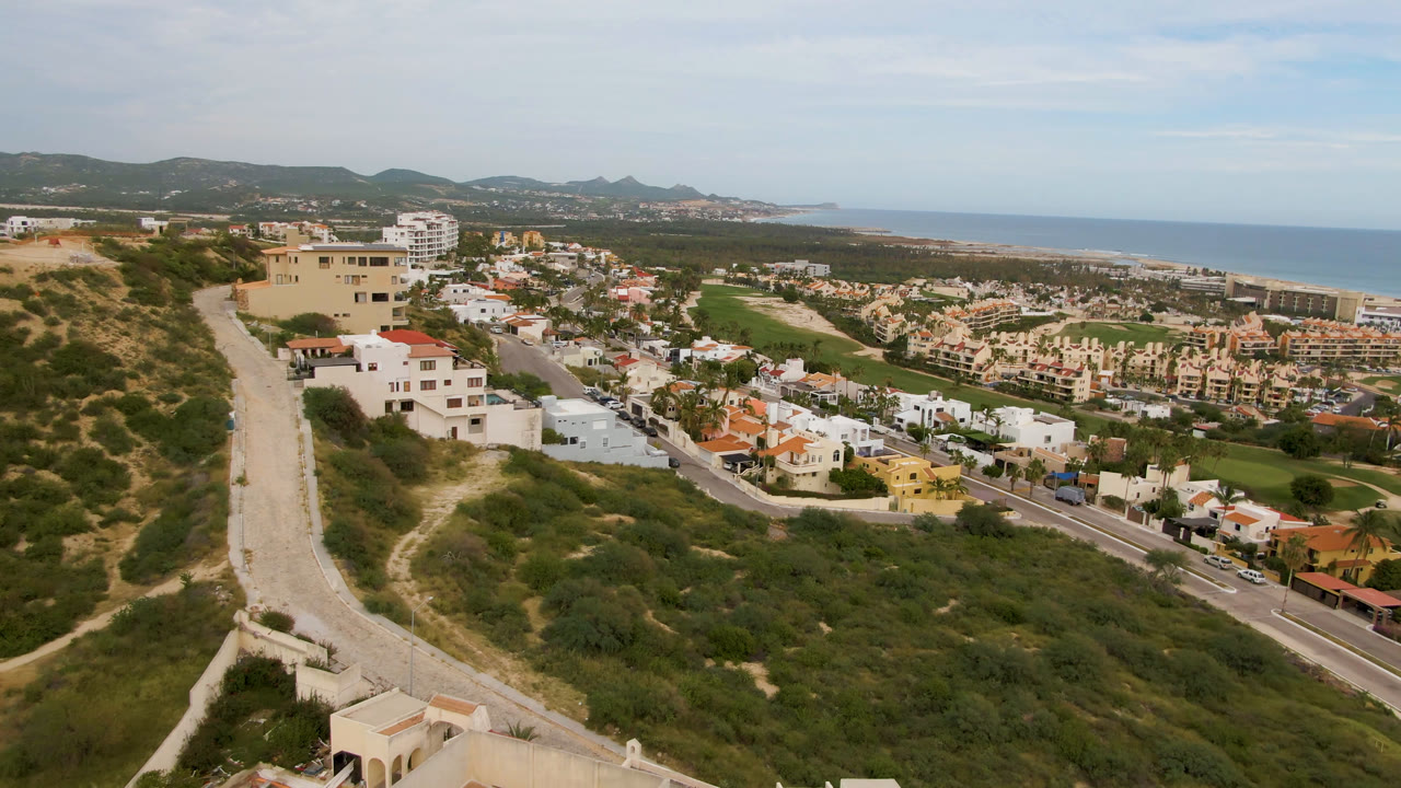 Aerial view of hillside roads, homes, golf-course greenery, and ocean horizon.