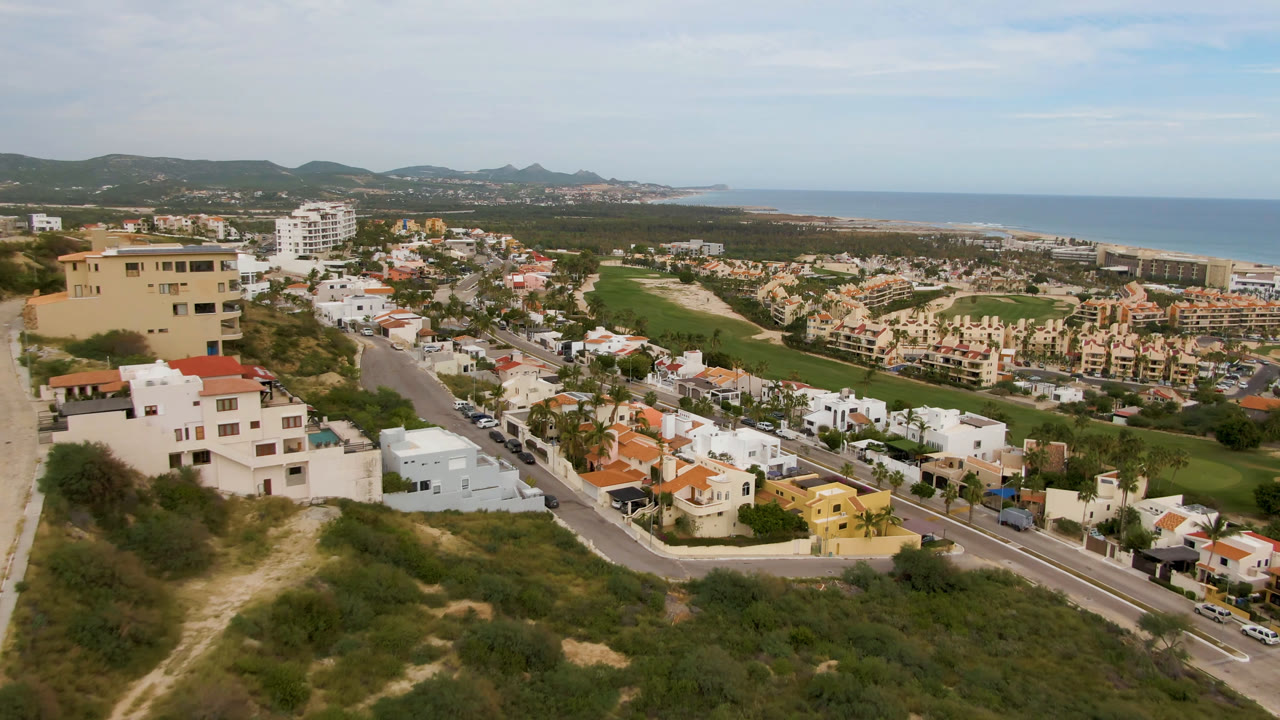 Aerial view over hillside homes, road, golf course, coastline, and ocean.
