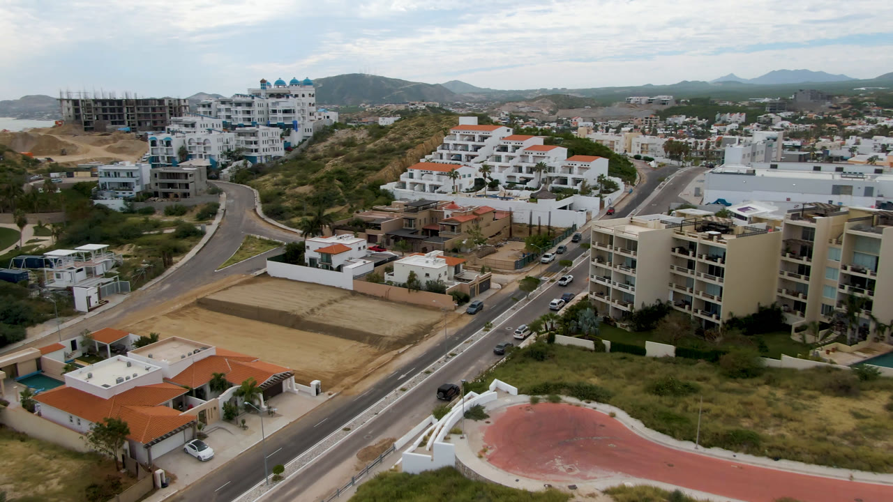 Aerial view over homes, roads, a field, hills, and distant coastline.