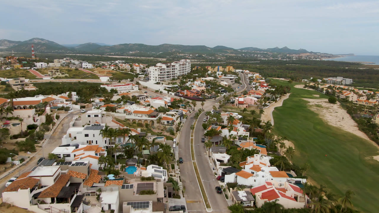 Drone view of golf fairway, villas, road, and hazy coastal horizon.