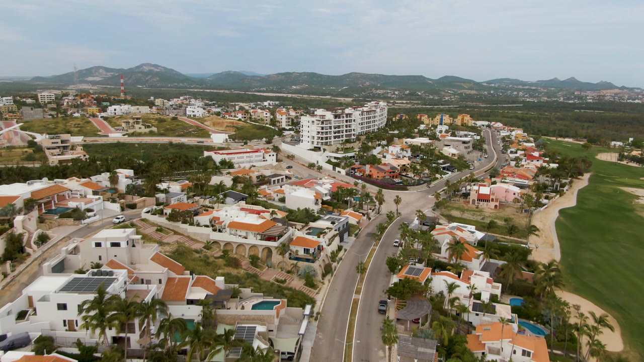 Aerial view of houses, a curved road, greenery, and distant hills.