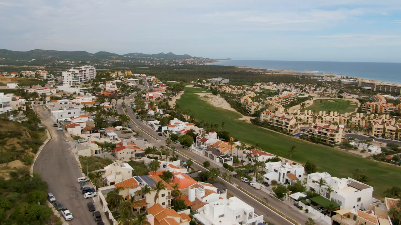 Aerial view of homes, road, golf course, hills, and ocean.