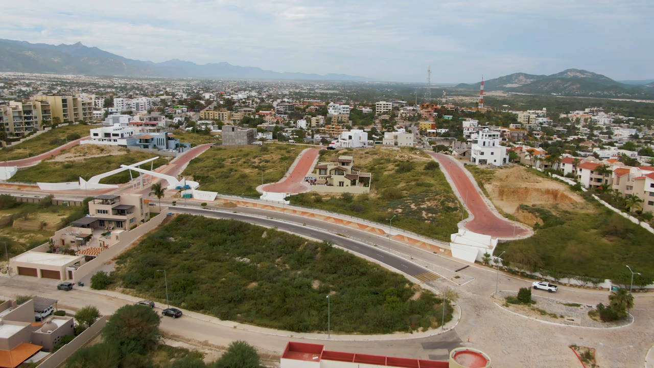 Aerial view of a divided road, red path, hillside homes, and distant mountains.