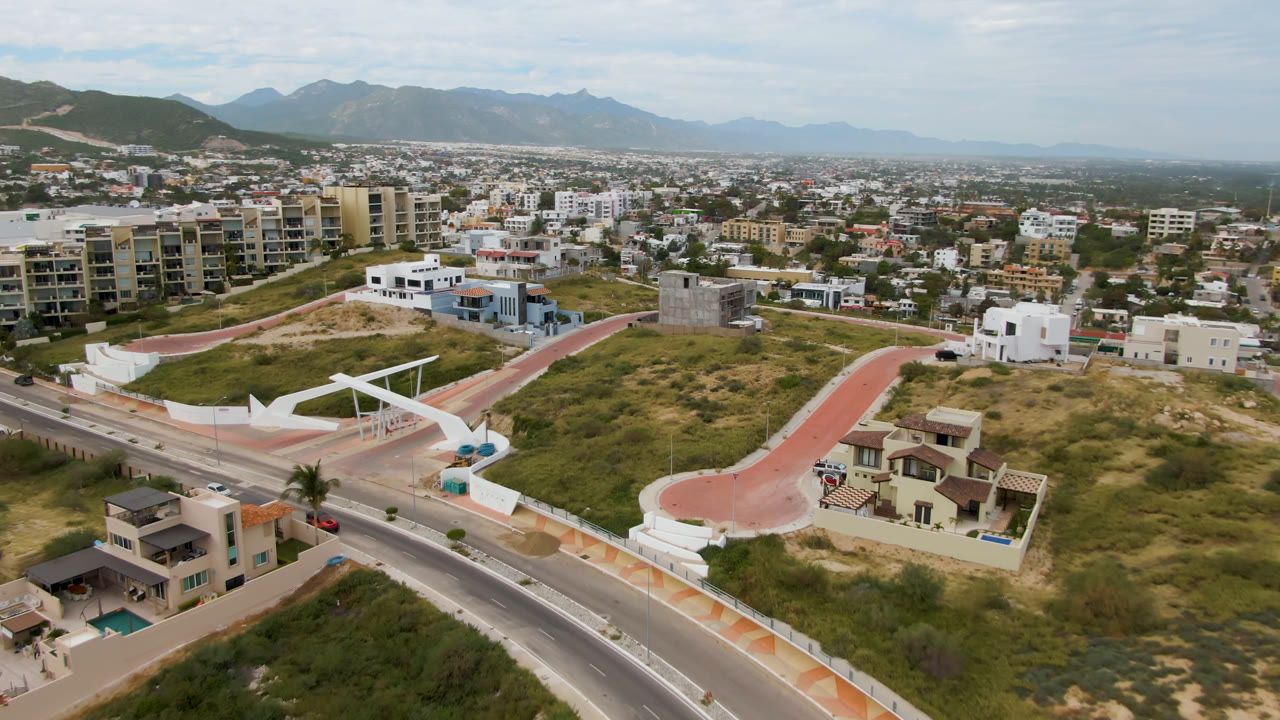 Aerial view of a road, hillside homes, vacant lots, and distant mountains.