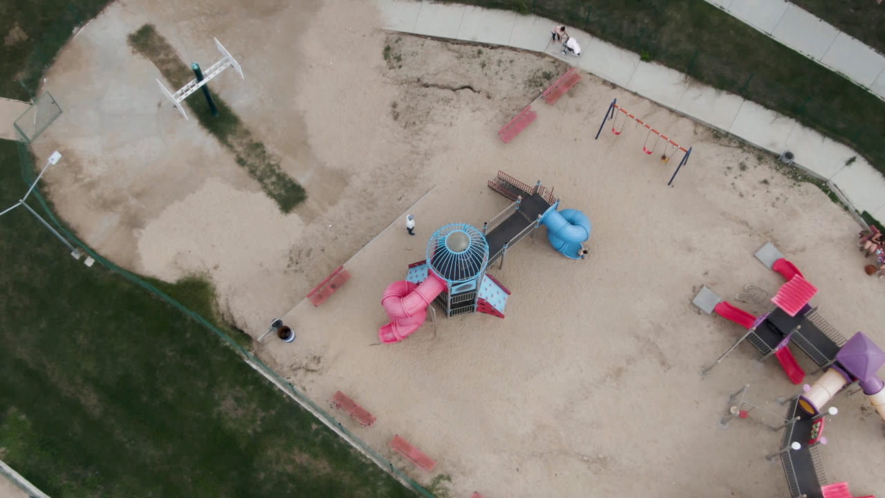 Aerial view of sandy playground beside grass and paved paths.