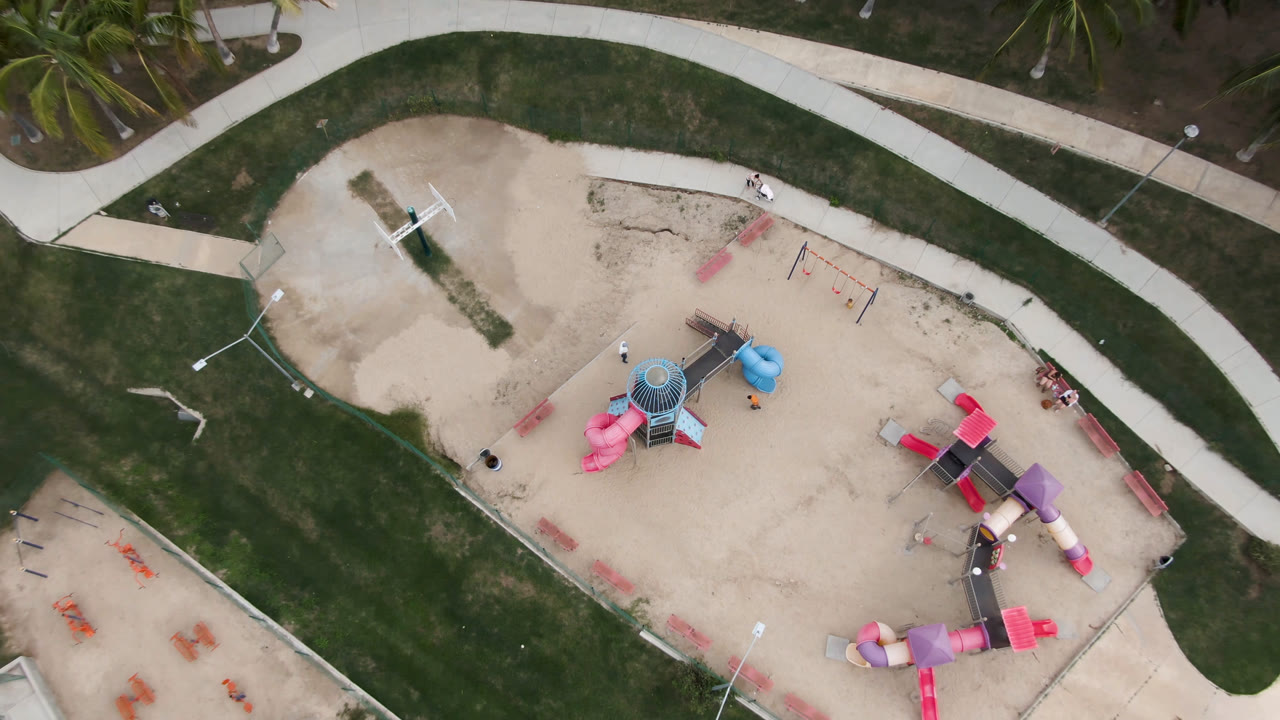 Aerial view of an empty playground with colorful equipment and a path above it.