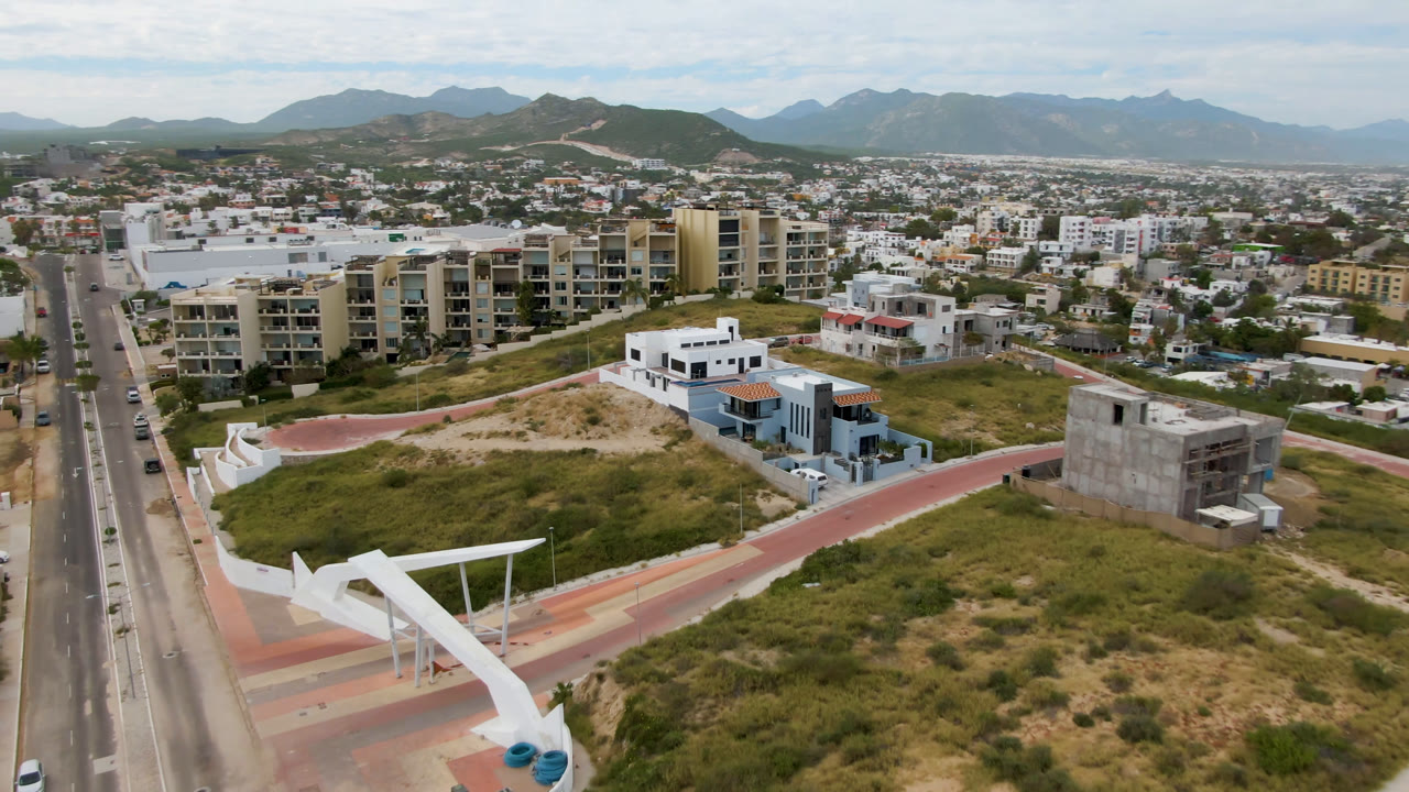 Aerial view of a divided road beside apartment buildings, homes, open scrub lots, and distant mountains.
