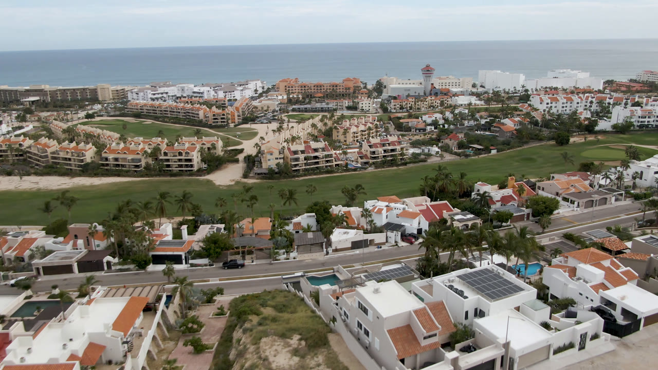 Aerial view of white-roofed homes, a golf course, resort buildings, and ocean horizon.