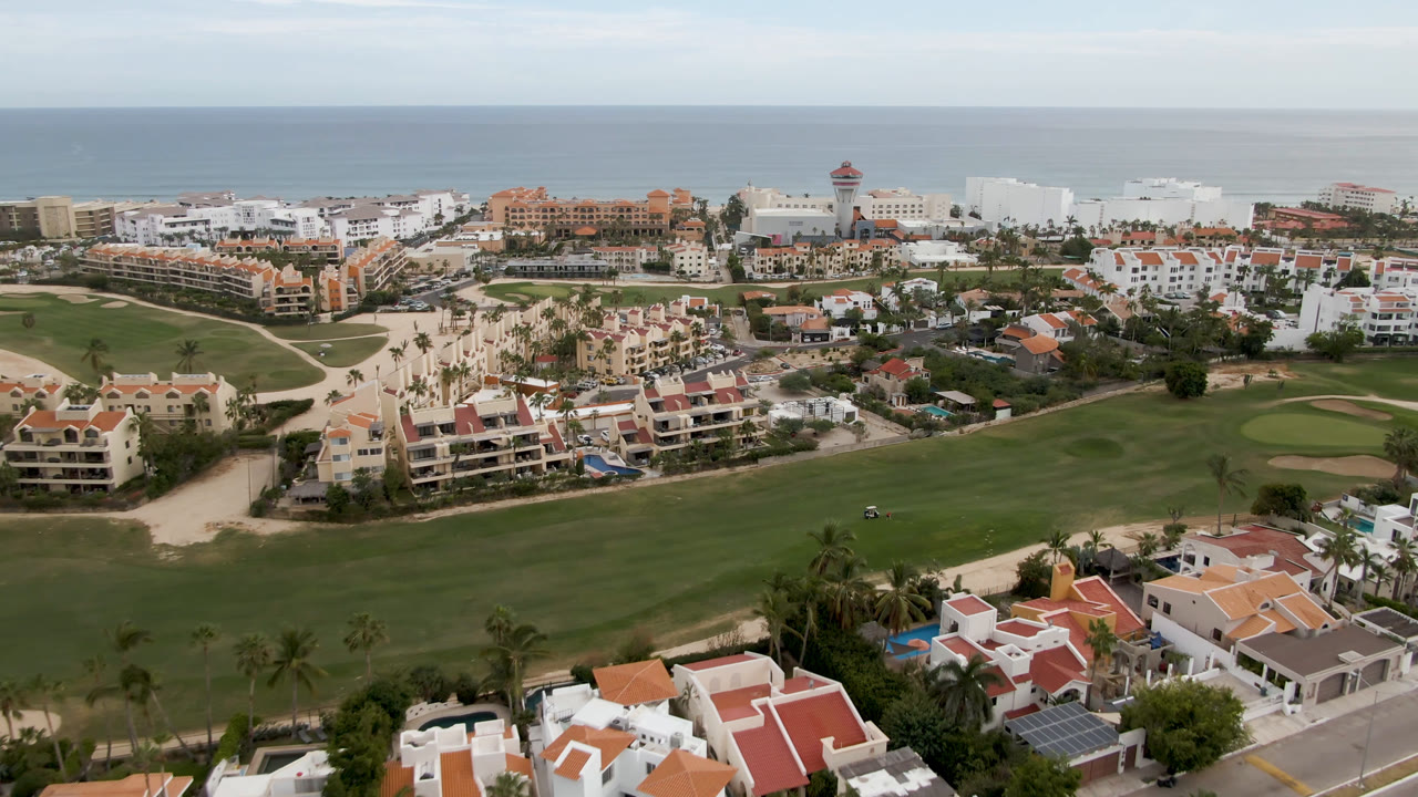 Aerial view over a golf course, resort buildings, and ocean horizon.