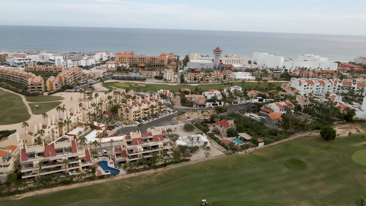 Aerial view of coastal resort buildings, golf course, beach, and ocean horizon.