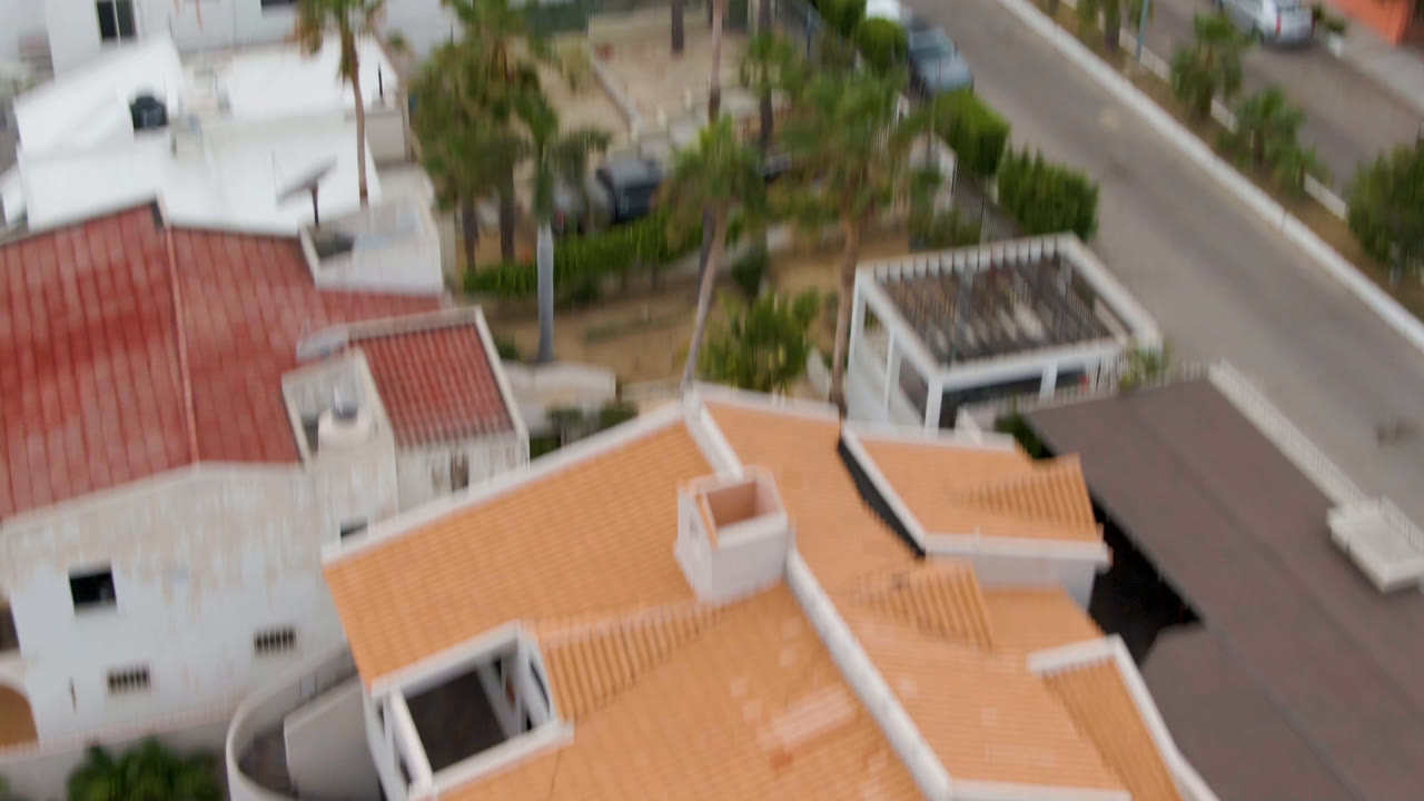 The second frame looks down over San Jose del Cabo homes with tile roofs, a narrow street edge, courtyard walls, palms, and no visible people.