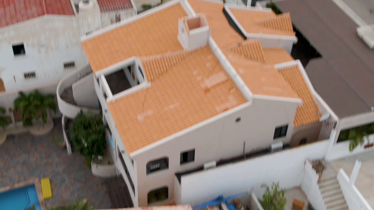 Drone angle above a white house with an orange tile roof and adjacent street.