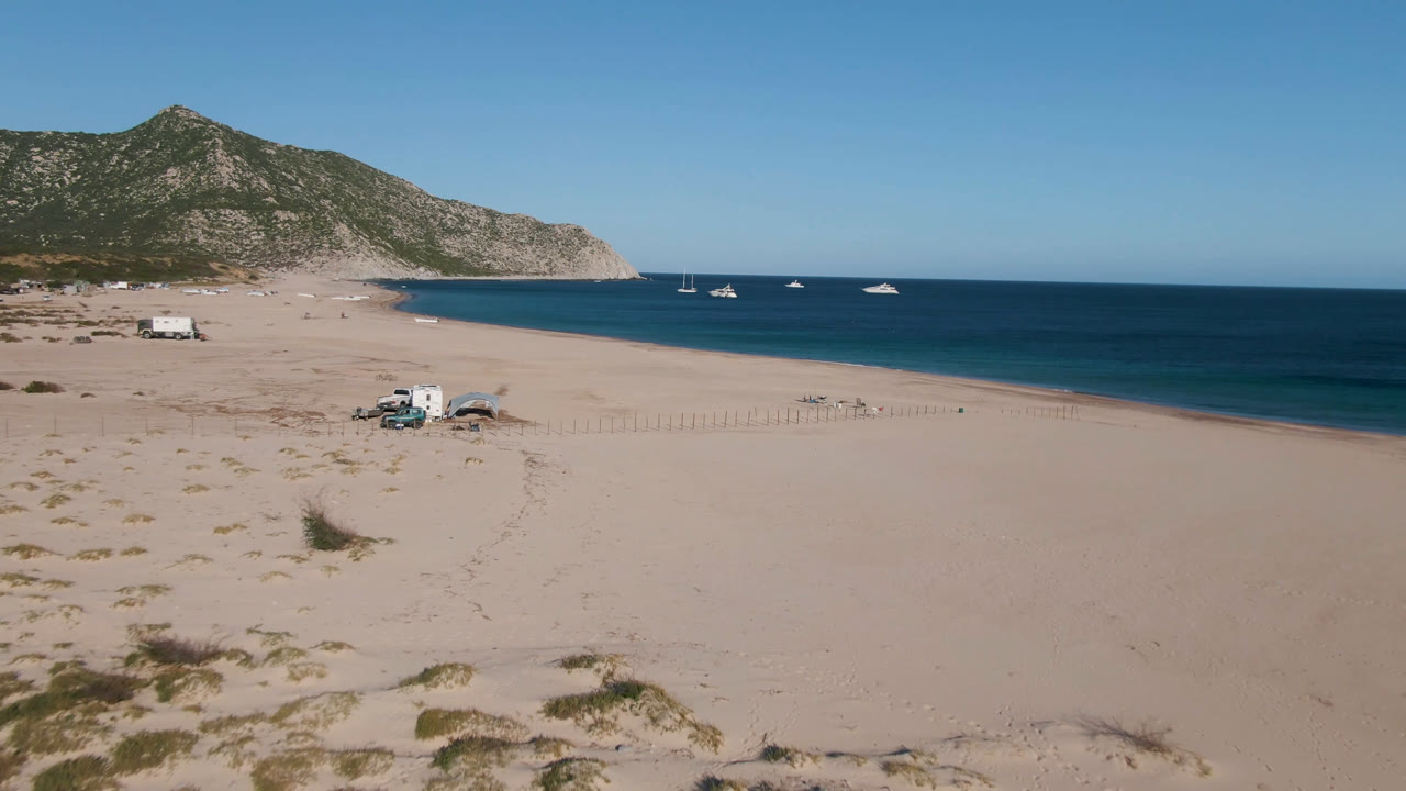 Sandy beach and dark blue water with several anchored boats near a rocky coast.