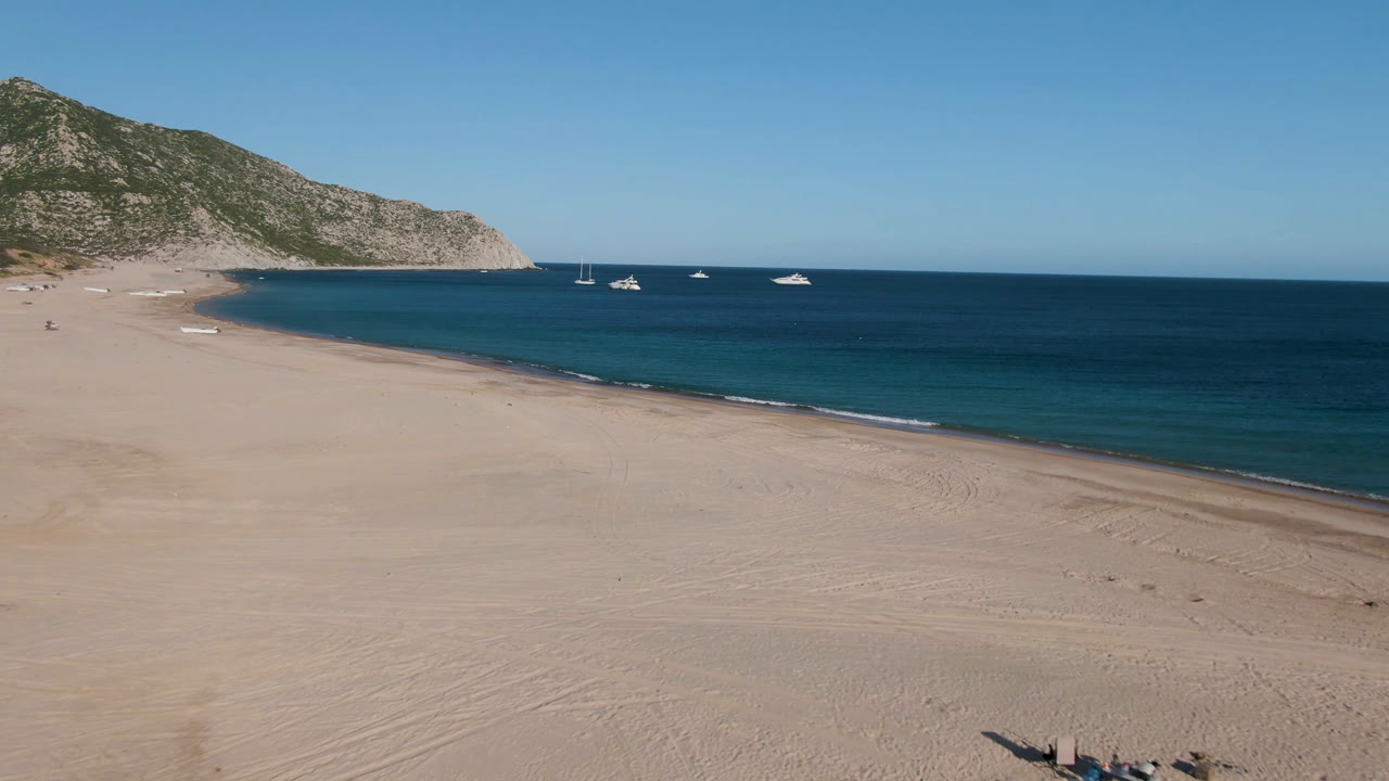 Open beach and shoreline with small boats anchored beyond the surf.