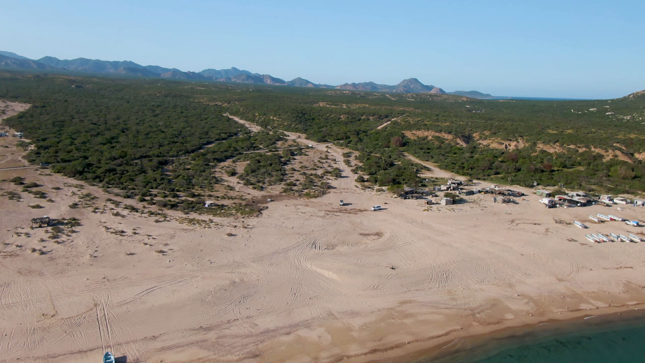 Drone view across beach tents, scrubland, and distant coast