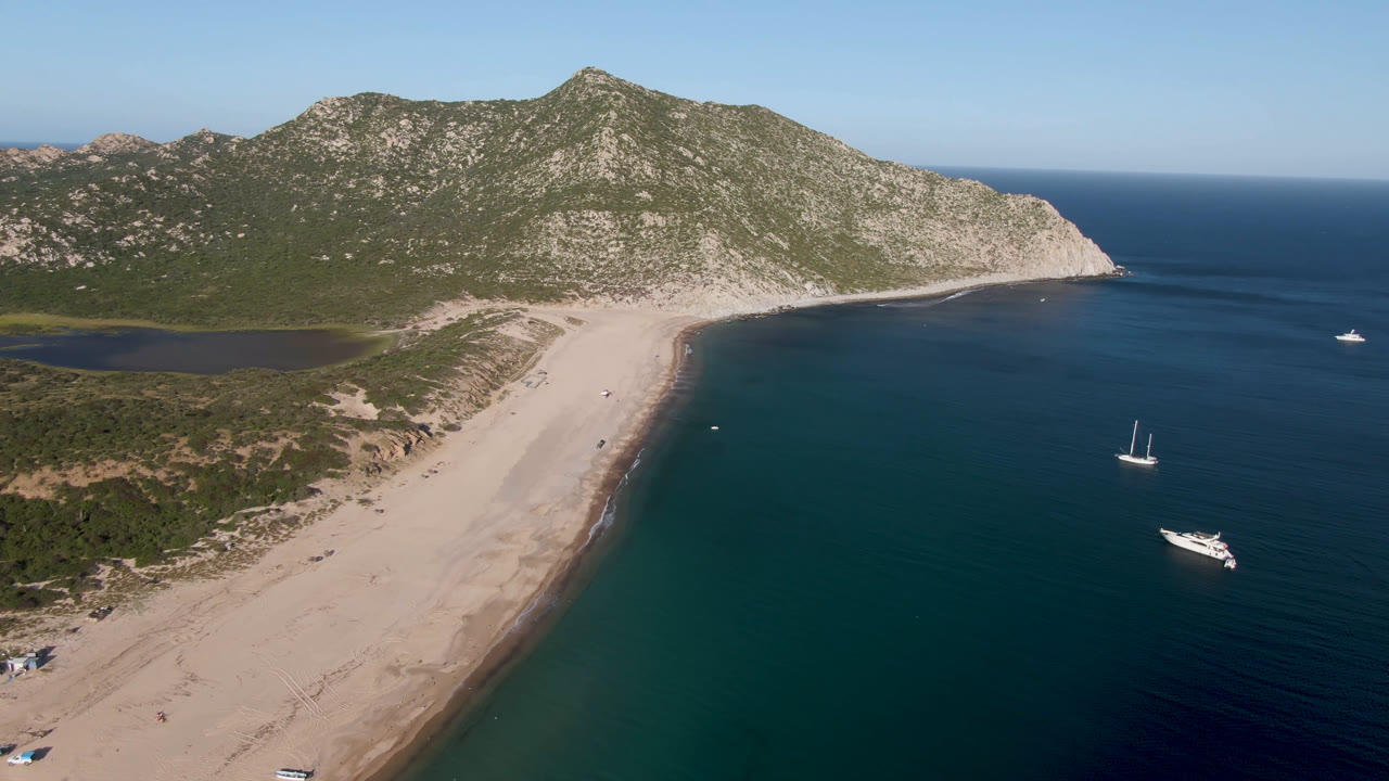Aerial view of Los Frailes with pale sand extending along the shore, small boats spaced across the water, a sailboat near mid-right, and no visible people.