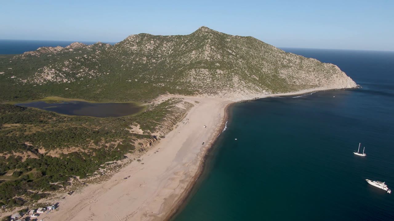 Wide aerial of Los Frailes beach, green hills, ocean horizon, and offshore boats.