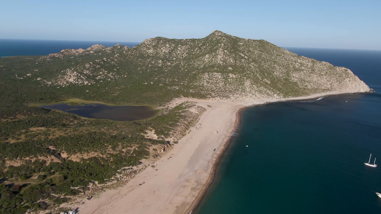 Aerial view of a sandy beach, lagoon, ocean, and mountain ridge.