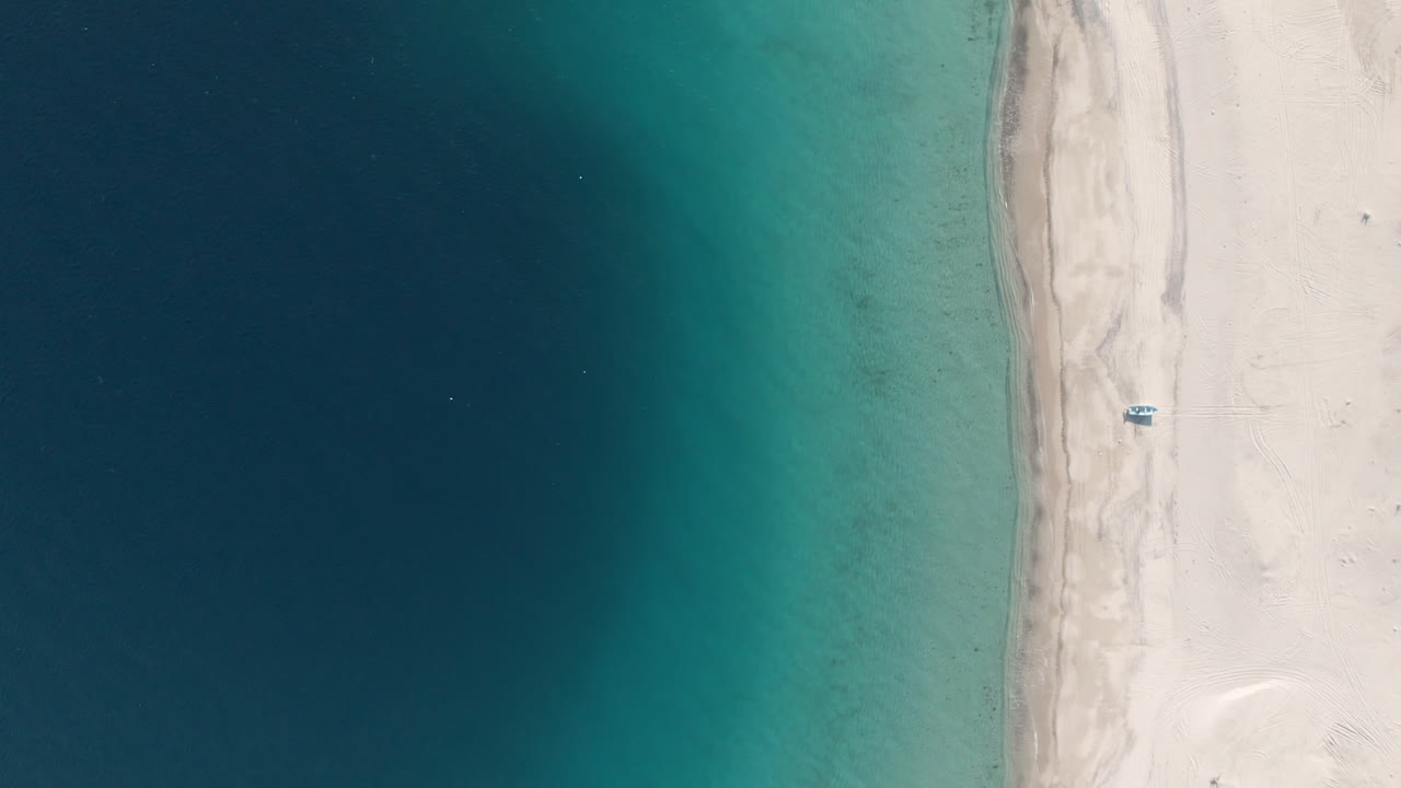 Overhead beach with turquoise water, pale sand, and a small boat near shore.