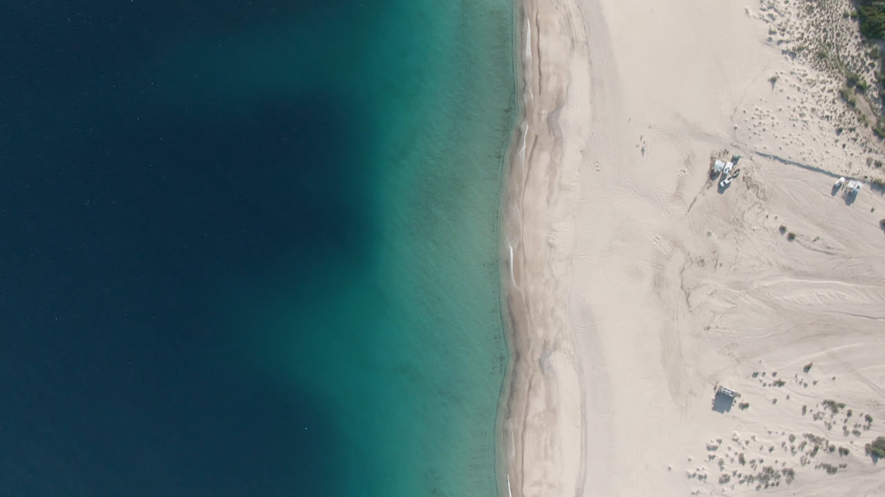 Top-down shoreline with blue water and beach dunes.