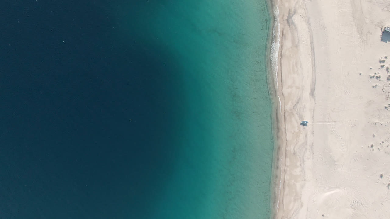 Top-down beach shoreline with turquoise water and a small boat near the sand.