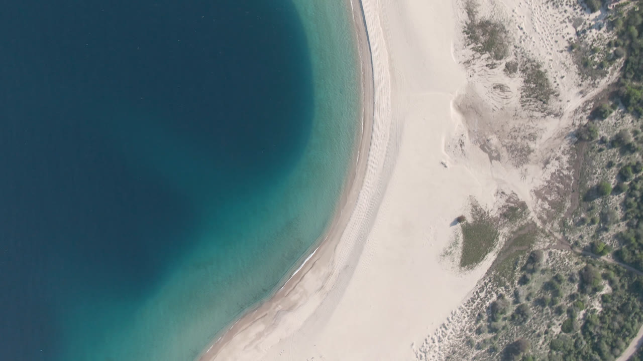 High aerial view of beach, water, dunes, and small structures.