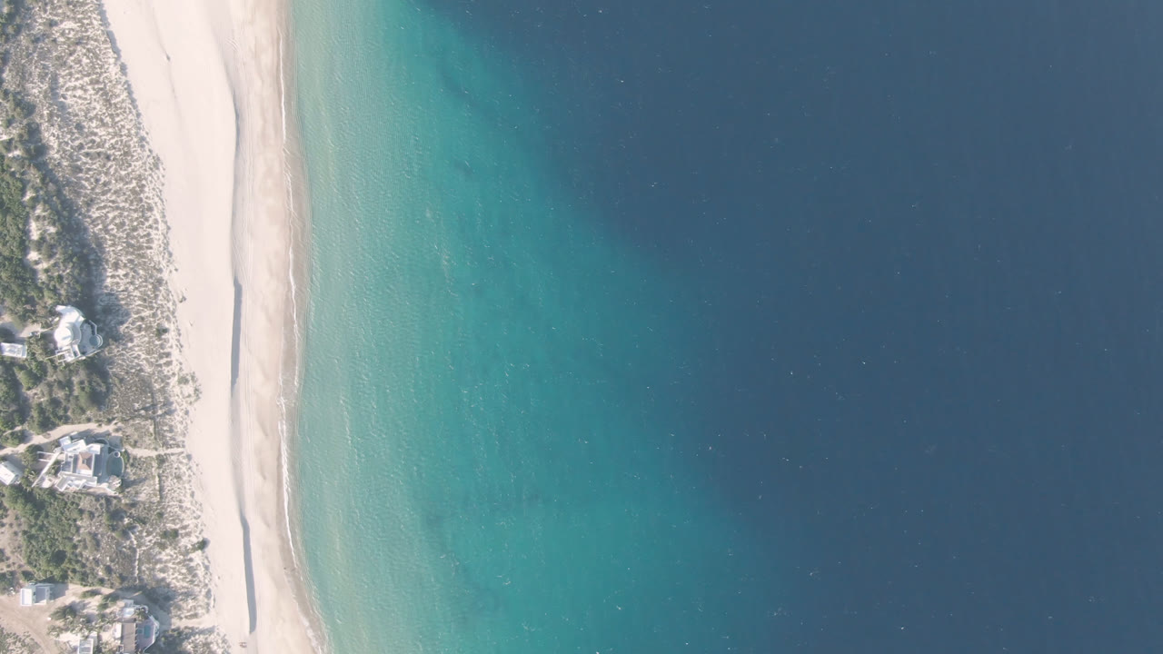 Overhead beach and blue water with coastal buildings at the edge