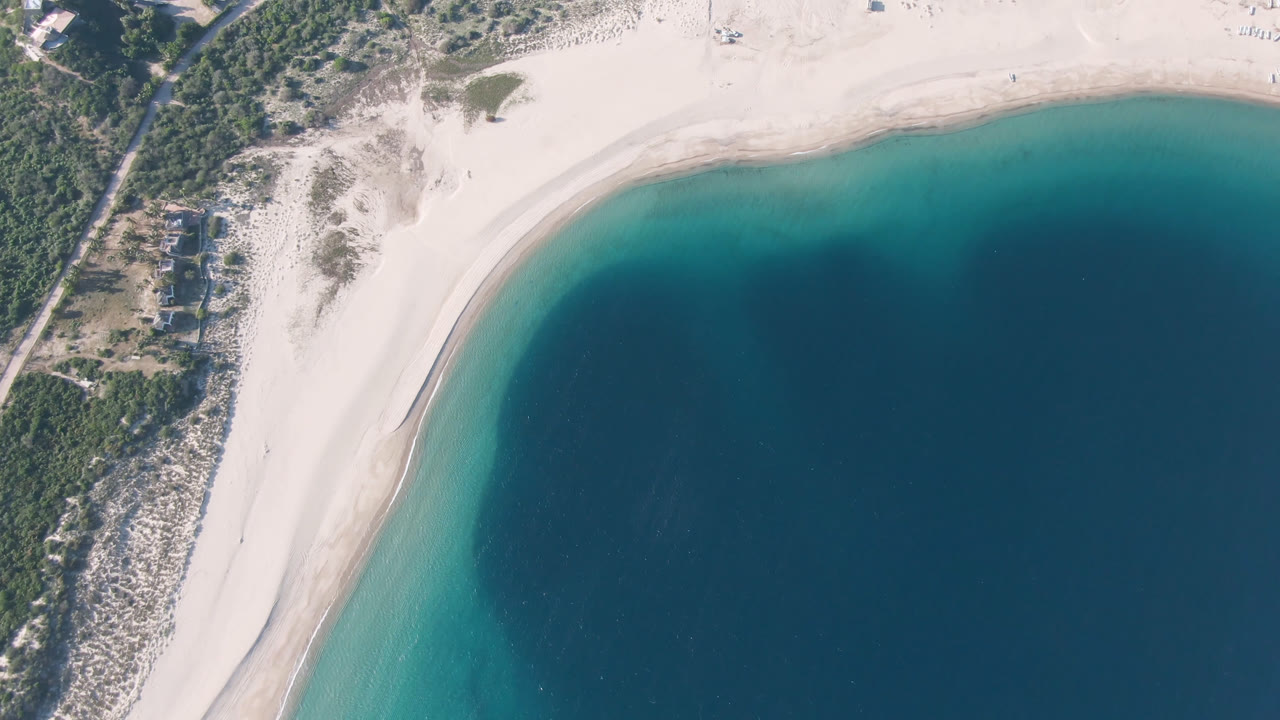 Aerial view of a curved beach beside blue ocean and coastal vegetation.