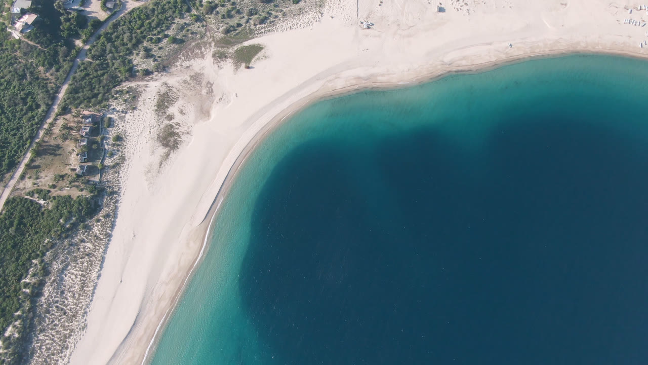 Aerial frame over Los Frailes with the shoreline shifted slightly across the view, showing pale sand, a narrow surf line, teal shallows, deep blue water, and no visible people.